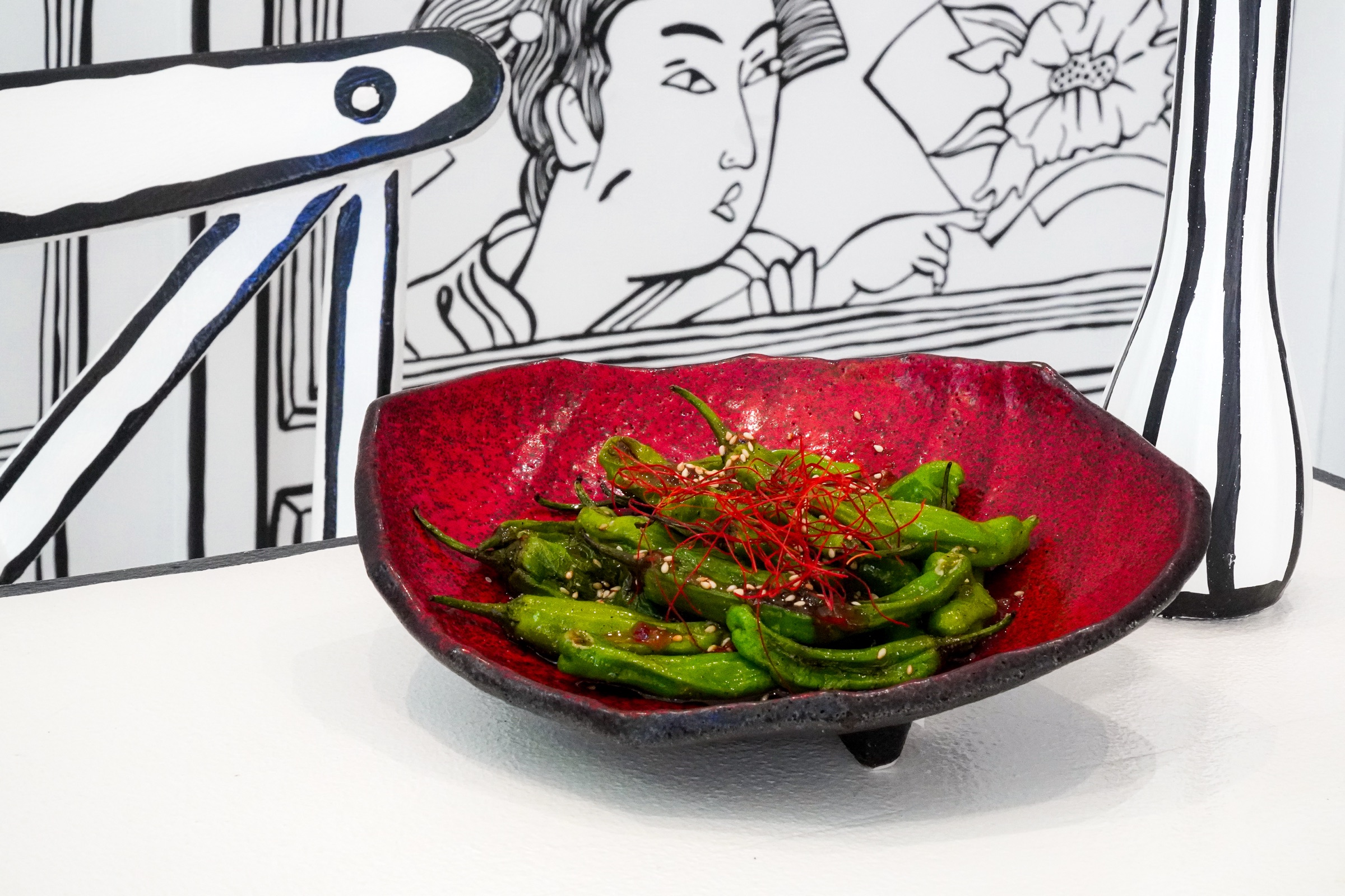 Shishito peppers in a red bowl with the dining room linework behind.